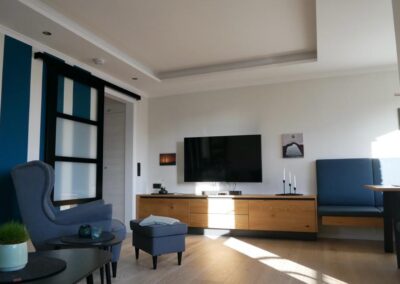 Das Wohnzimmer, Ohrensessel, Smart-Tv, Schiebetür, Holzfußboden, Sideboard-schränke mit Geschirr und Gesellschaftsspielen,
